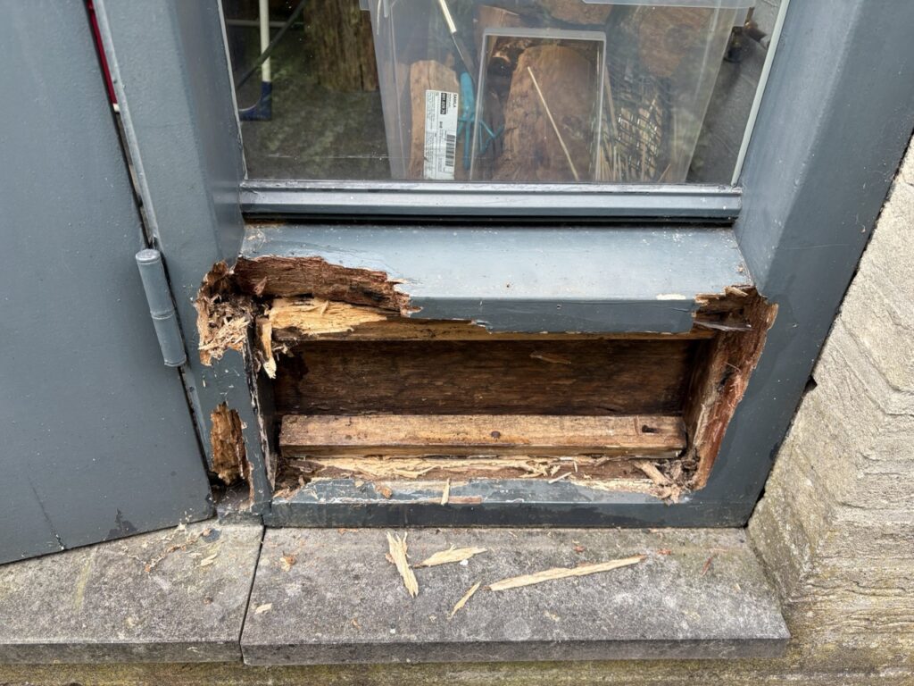 Diepe houtrot in houten onderdeel naast de voordeur onzichtbaar en aangetast